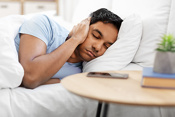 Image showing sleepy indian man in bed closing ear with hand