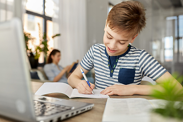 Image showing student boy with book writing to notebook at home