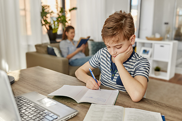 Image showing student boy with book writing to notebook at home