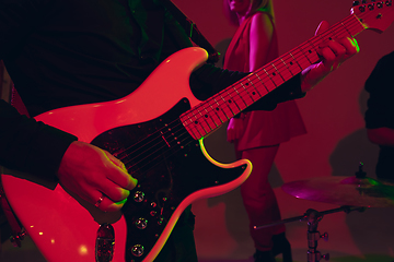 Image showing Young caucasian musician, band performing in neon light on red studio background