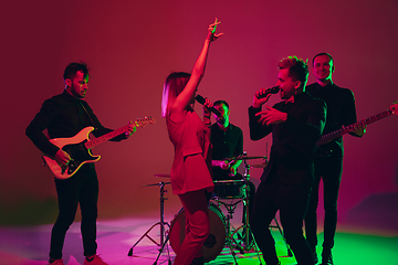 Image showing Young caucasian musicians, band performing in neon light on red studio background