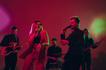 Image showing Young caucasian musicians, band performing in neon light on red studio background