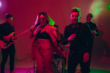 Image showing Young caucasian musicians, band performing in neon light on red studio background