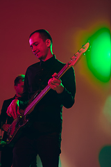 Image showing Young caucasian musician, band performing in neon light on red studio background