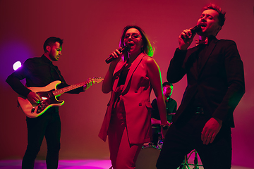 Image showing Young caucasian musicians, band performing in neon light on red studio background