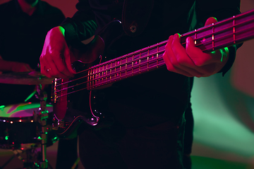 Image showing Young caucasian musician, band performing in neon light on red studio background