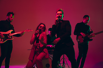 Image showing Young caucasian musicians, band performing in neon light on red studio background