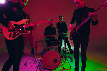 Image showing Young caucasian musicians, band performing in neon light on red studio background