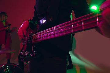 Image showing Young caucasian musician, band performing in neon light on red studio background