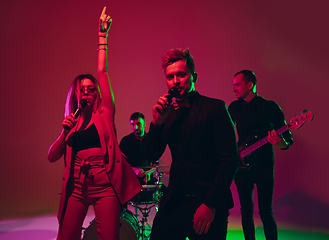 Image showing Young caucasian musicians, band performing in neon light on red studio background