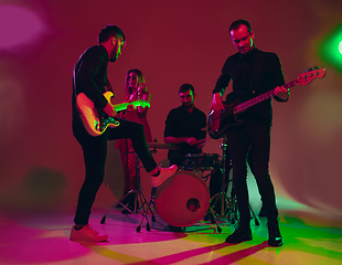 Image showing Young caucasian musicians, band performing in neon light on red studio background