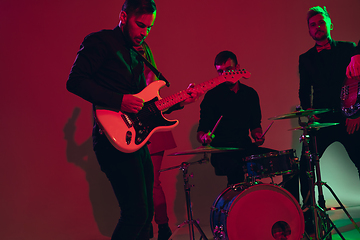 Image showing Young caucasian musicians, band performing in neon light on red studio background