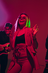 Image showing Young caucasian musician, singer performing in neon light on red studio background