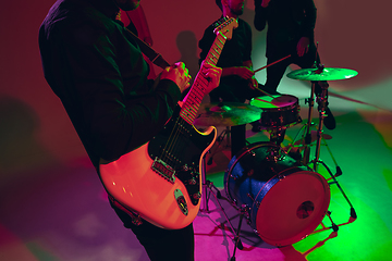 Image showing Young caucasian musician, band performing in neon light on red studio background