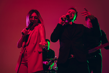 Image showing Young caucasian musicians, singers performing in neon light on red studio background