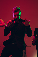 Image showing Young caucasian musician, singer performing in neon light on red studio background