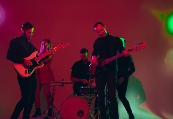 Image showing Young caucasian musicians, band performing in neon light on red studio background