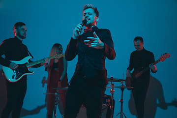 Image showing Young caucasian musicians, band performing in neon light on blue studio background, singer in front