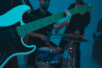 Image showing Young caucasian musicians, band performing in neon light on blue studio background, guitarist in front
