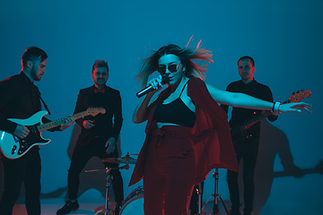 Image showing Young caucasian musicians, band performing in neon light on blue studio background, singer in front