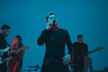 Image showing Young caucasian musicians, band performing in neon light on blue studio background, singer in front