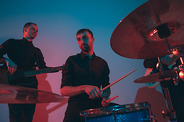 Image showing Young caucasian musicians, band performing in neon light on blue studio background