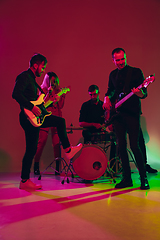 Image showing Young caucasian musicians, band performing in neon light on red studio background