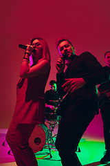 Image showing Young caucasian musicians, singers performing in neon light on red studio background