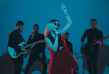 Image showing Young caucasian musicians, band performing in neon light on blue studio background, singer in front