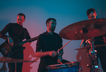 Image showing Young caucasian musicians, band performing in neon light on blue studio background
