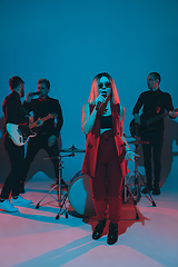 Image showing Young caucasian musicians, band performing in neon light on blue studio background, singer in front