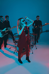 Image showing Young caucasian musicians, band performing in neon light on blue studio background, singer in front