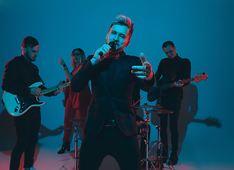 Image showing Young caucasian musicians, band performing in neon light on blue studio background, singer in front