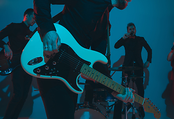 Image showing Young caucasian musicians, band performing in neon light on blue studio background, guitarist in front