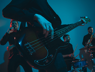 Image showing Young caucasian musicians, band performing in neon light on blue studio background, guitarist in front