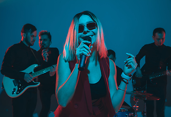 Image showing Young caucasian musicians, band performing in neon light on blue studio background, singer in front