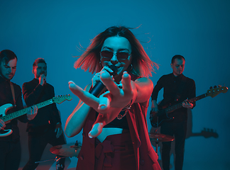 Image showing Young caucasian musicians, band performing in neon light on blue studio background, singer in front