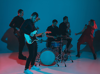 Image showing Young caucasian musicians, band performing in neon light on blue studio background, guitarist in front