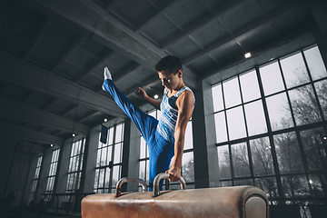 Image showing Little male gymnast training in gym, flexible and active. Caucasian fit little boy, athlete in sportswear practicing in exercises for strength, balance.