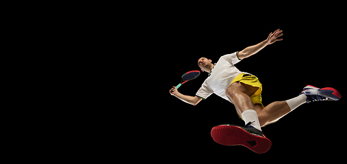 Image showing Young caucasian tennis player in action, motion isolated on black background, look from the bottom. Concept of sport, movement, energy and dynamic.