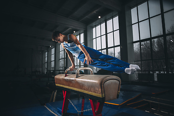 Image showing Little male gymnast training in gym, flexible and active. Caucasian fit little boy, athlete in sportswear practicing in exercises for strength, balance.