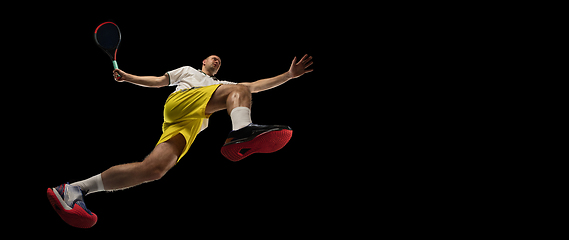 Image showing Young caucasian tennis player in action, motion isolated on black background, look from the bottom. Concept of sport, movement, energy and dynamic.