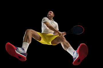 Image showing Young caucasian tennis player in action, motion isolated on black background, look from the bottom. Concept of sport, movement, energy and dynamic.