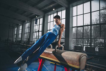 Image showing Little male gymnast training in gym, flexible and active. Caucasian fit little boy, athlete in sportswear practicing in exercises for strength, balance.