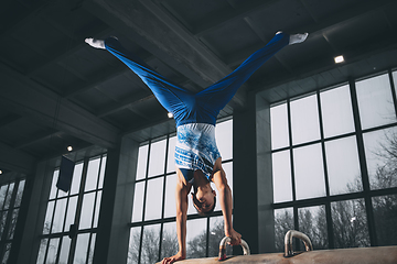 Image showing Little male gymnast training in gym, flexible and active. Caucasian fit little boy, athlete in sportswear practicing in exercises for strength, balance.