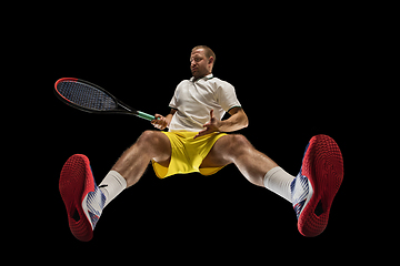 Image showing Young caucasian tennis player in action, motion isolated on black background, look from the bottom. Concept of sport, movement, energy and dynamic.