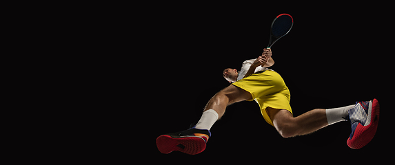 Image showing Young caucasian tennis player in action, motion isolated on black background, look from the bottom. Concept of sport, movement, energy and dynamic.