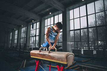 Image showing Little male gymnast training in gym, flexible and active. Caucasian fit little boy, athlete in sportswear practicing in exercises for strength, balance.