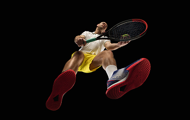 Image showing Young caucasian tennis player in action, motion isolated on black background, look from the bottom. Concept of sport, movement, energy and dynamic.