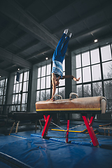 Image showing Little male gymnast training in gym, flexible and active. Caucasian fit little boy, athlete in sportswear practicing in exercises for strength, balance.